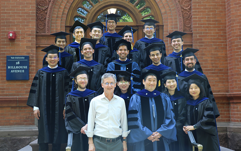 The Class of 2024 with Tony Smith and Yuichi Kitamura in their caps and gowns on the steps outside 28 Hillhouse Ave