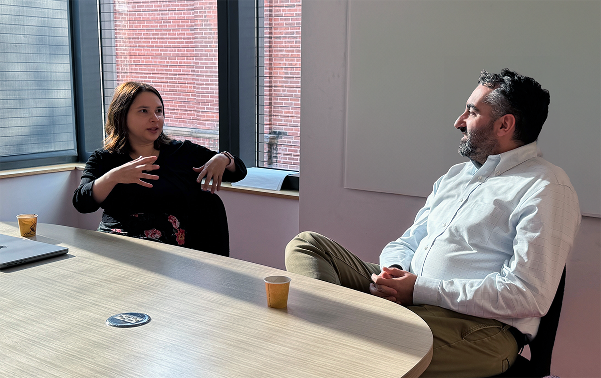 A woman in a black shirt sits down at a table with a man in a white shirt, having an animated conversation