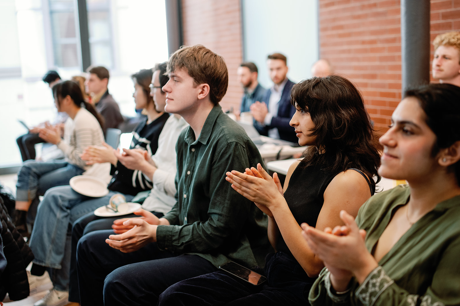 A row of students applaud at the conclusion of a presentation