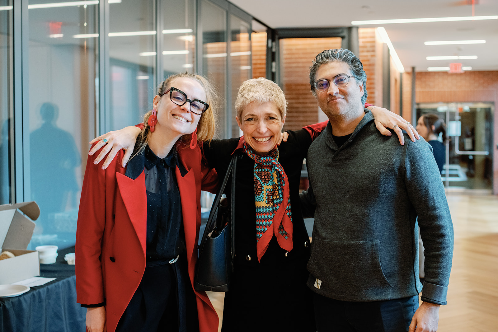 A woman in a red jacket, a woman in a black sweater, and a man in a grey sweater pose for a group photo