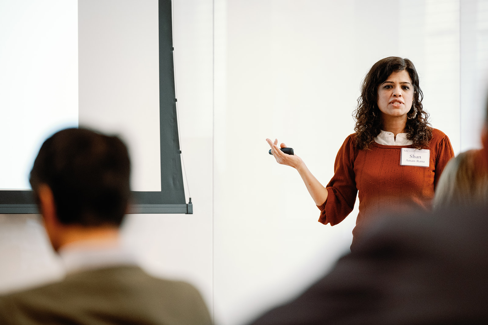 A woman in a red shirt presents a paper in front of an audience
